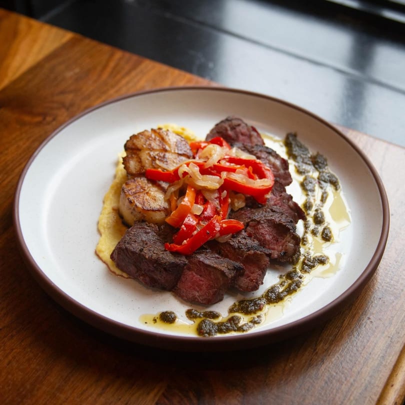 Butcher Bar's steak and scallops with roasted peppers and onions on a white plate.