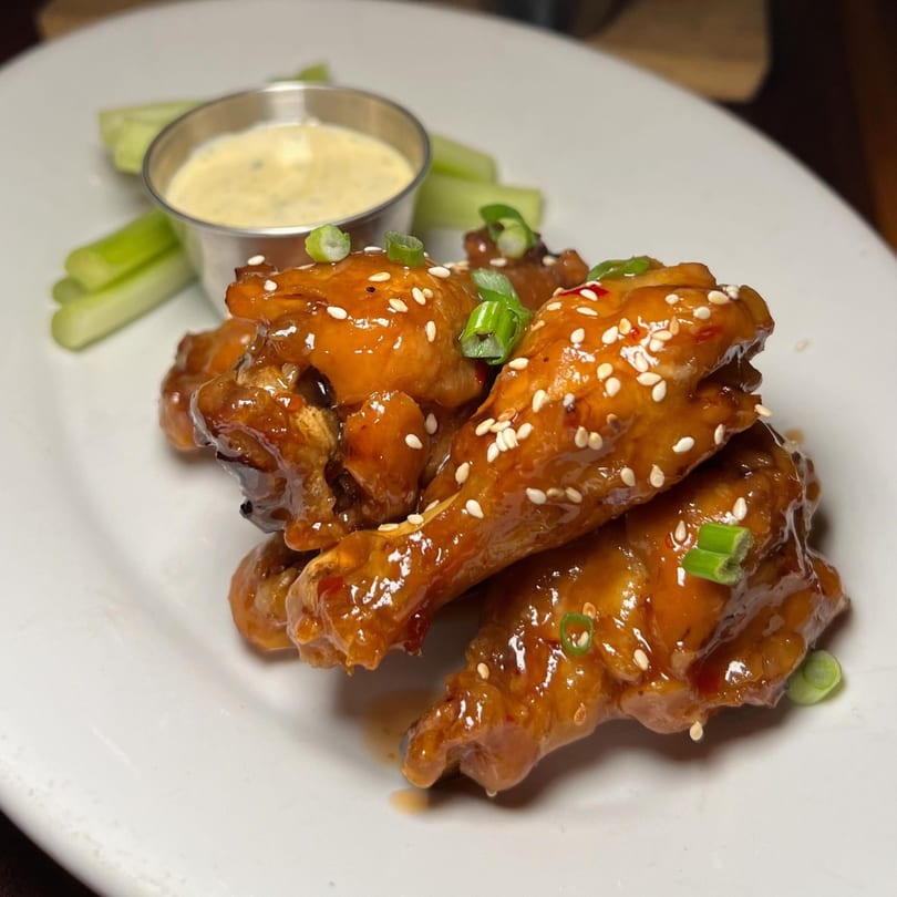 Butcher Bar's sticky glazed chicken wings with sesame seeds, scallions, celery sticks, and dipping sauce.